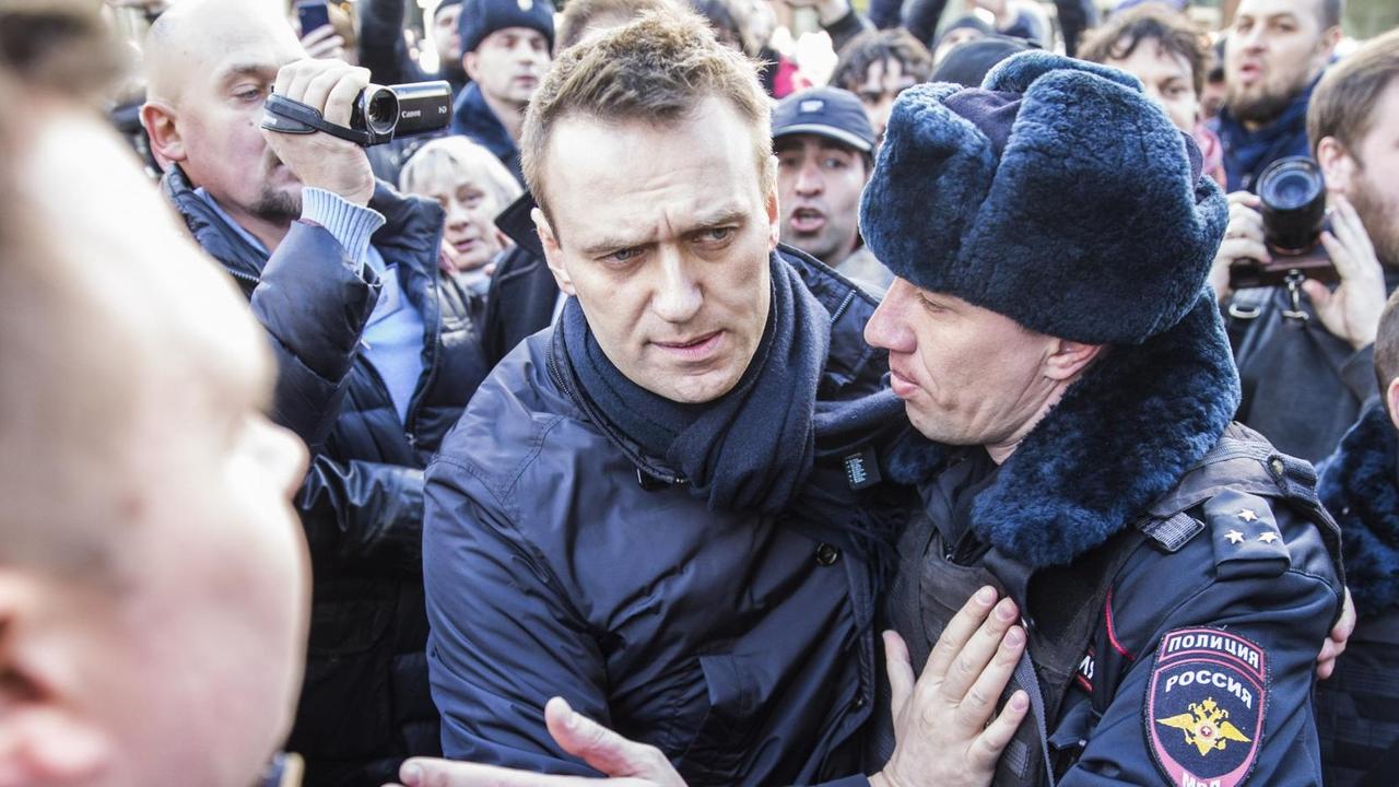 Zwei Polizisten führen Nawalny aus einer Menge von Demonstranten, von denen einige die Szene filmen bzw. fotografieren. Zwei Polizisten führen Nawalny aus einer Menge von Demonstranten, von denen einige die Szene filmen bzw. fotografieren.