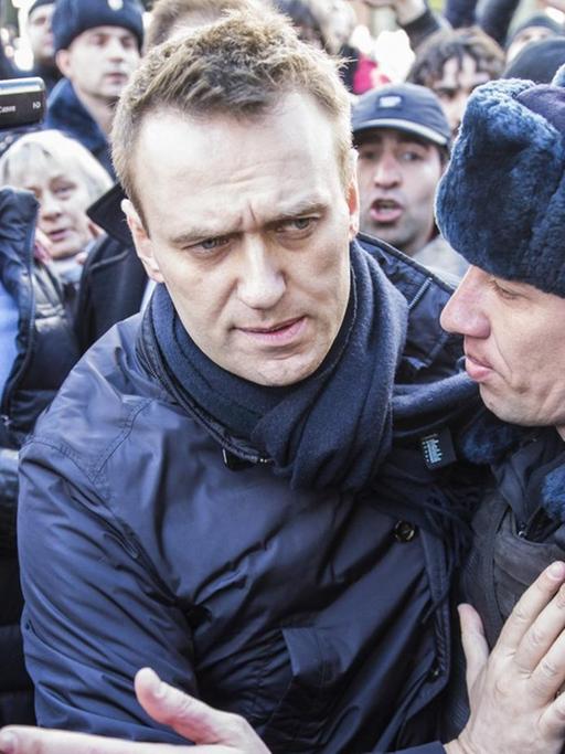 Zwei Polizisten führen Nawalny aus einer Menge von Demonstranten, von denen einige die Szene filmen bzw. fotografieren.