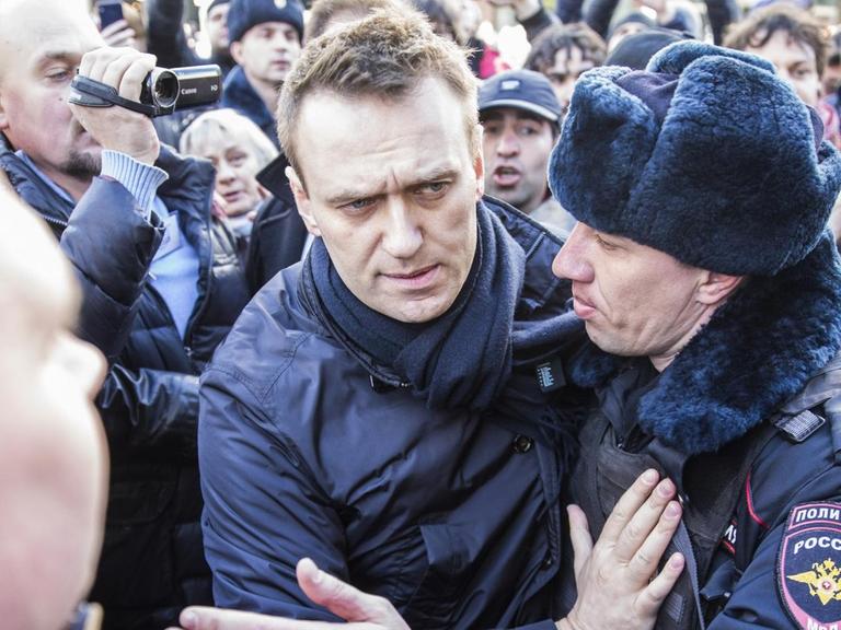 Zwei Polizisten führen Nawalny aus einer Menge von Demonstranten, von denen einige die Szene filmen bzw. fotografieren.