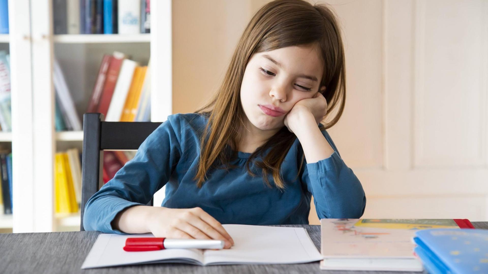 Ein Mädchen sitzt mit genervtem Gesichtsausdruck vor seinen Hausaufgaben.
