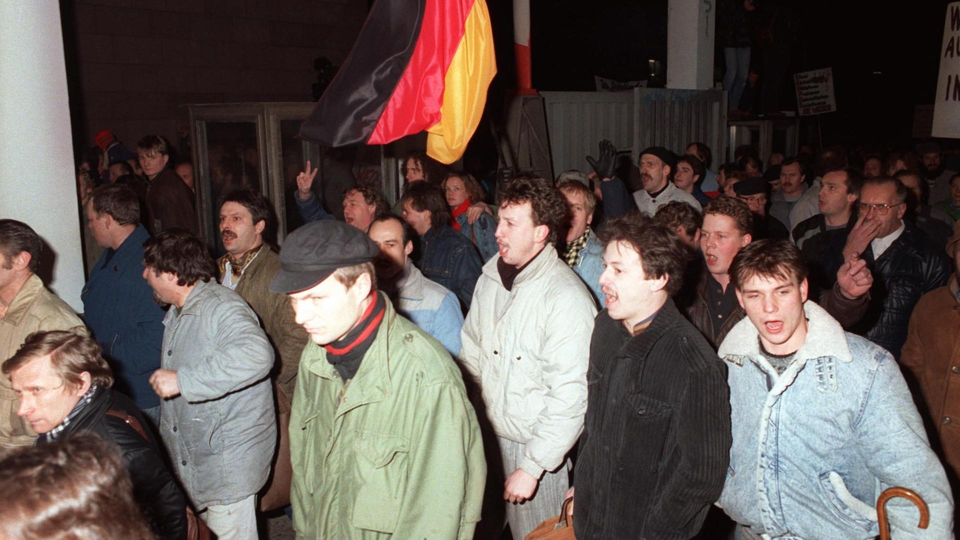 Demonstranten gehen am 15.01.1990 in Ostberlin mit einer Deutschland-Fahne durch ein Tor auf das Gelände der Stasi-Zentrale (Ministerium für Staatssicherheit der DDR, MfS). Demonstranten gehen am 15.01.1990 in Ostberlin mit einer Deutschland-Fahne durch ein Tor auf das Gelände der Stasi-Zentrale (Ministerium für Staatssicherheit der DDR, MfS).
