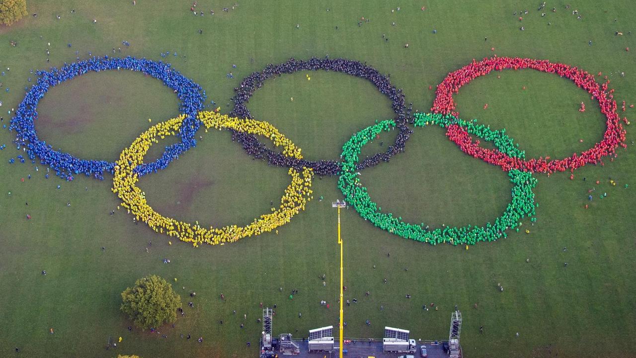 Hunderte Menschen in bunten Ponchos bilden im Stadtpark in Hamburg die Olympischen Ringe. Gegner haben davor das Wort "No" gebildet.