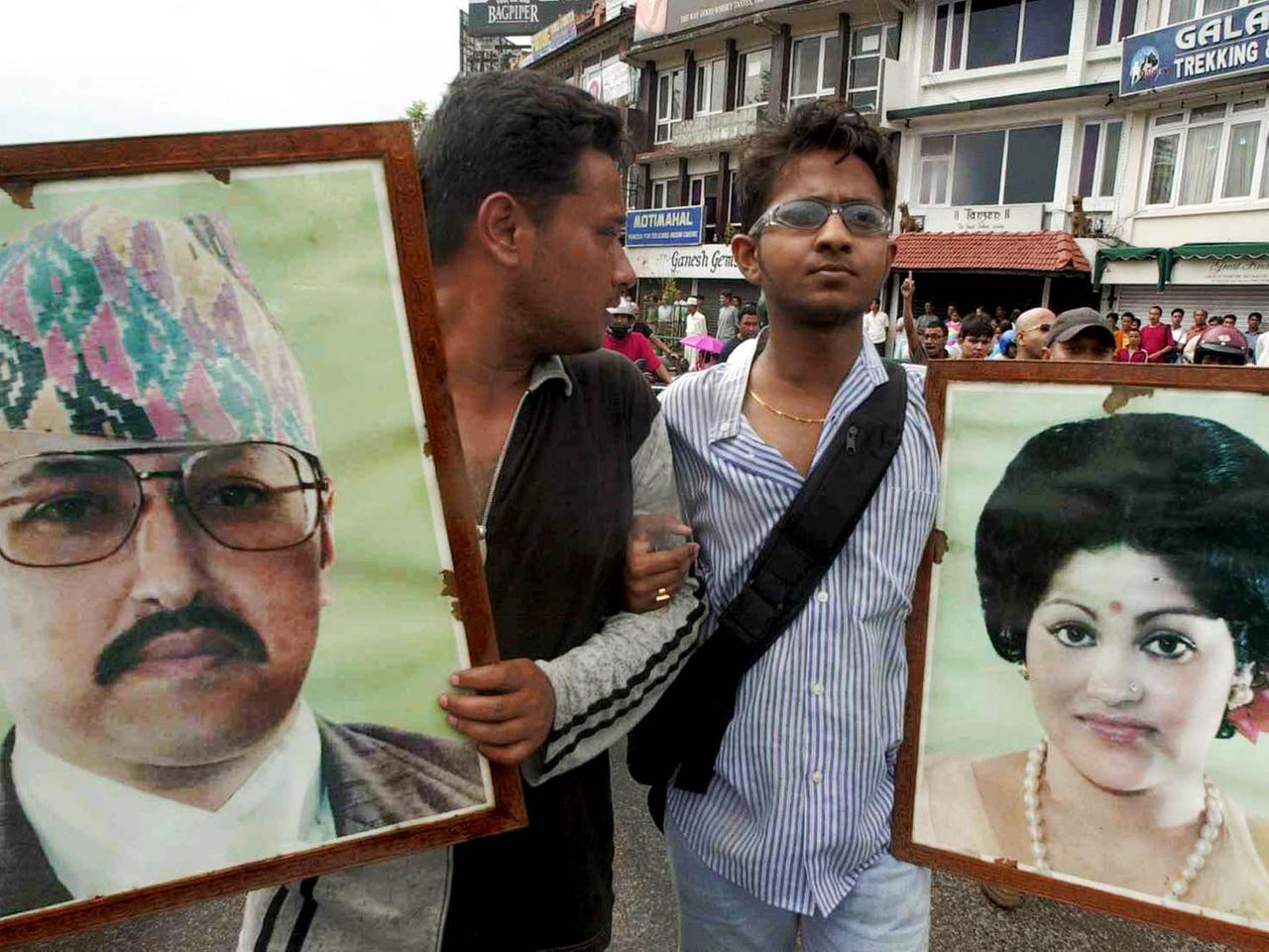 Zwei junge Männer stehen auf einer Straße und halten große Bilder von König Birendra und Königin Aishwarya in den Händen.