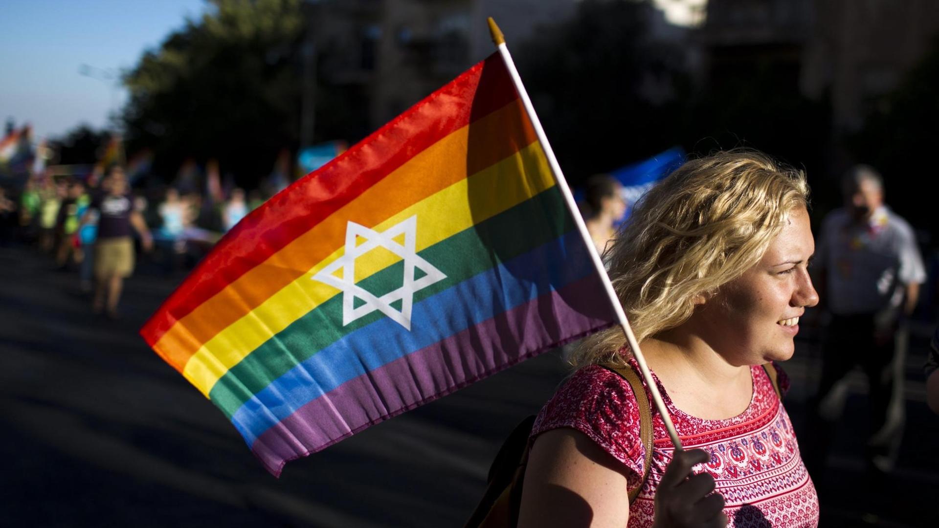 Eine Frau hält während einer Gay-Pride-Parade in Jerusalem 2016 eine Regenbogenfahne mit einem Davidstern in der Mitte in der Hand. Eine Frau hält während einer Gay-Pride-Parade in Jerusalem 2016 eine Regenbogenfahne mit einem Davidstern in der Mitte in der Hand.