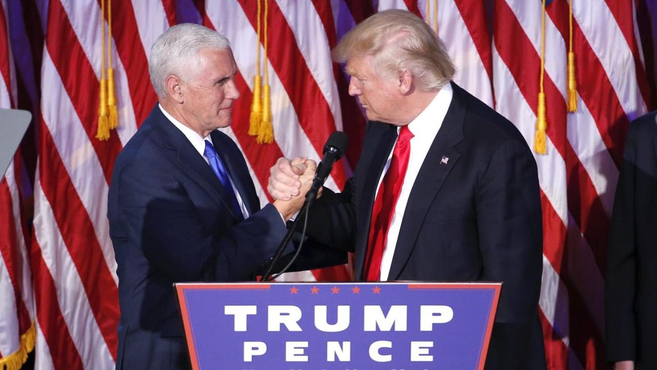 Donald Trump und sein Vizepräsident Mike Pence schütteln Hände auf einer Bühne