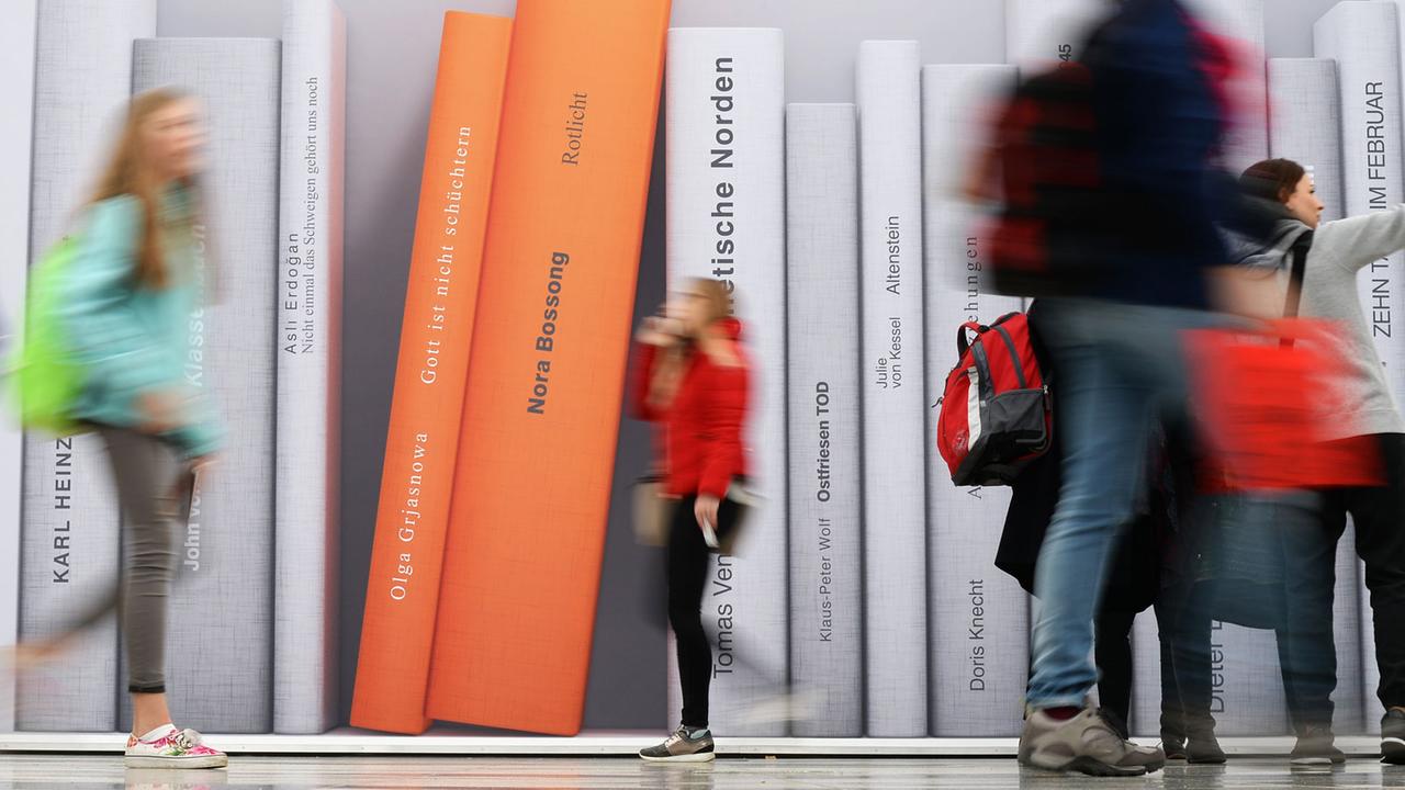 Besucher der Leipziger Buchmesse gehen an einer Fotowand vorbei, auf der überdimensionale Bücher abgebildet sind. Besucher der Leipziger Buchmesse gehen an einer Fotowand vorbei, auf der überdimensionale Bücher abgebildet sind.