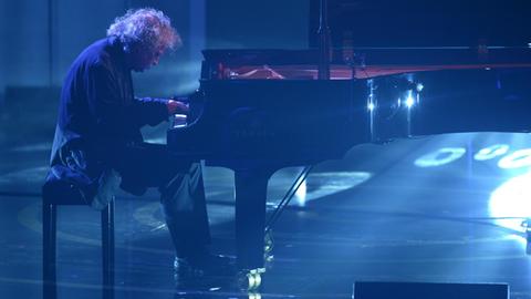 Der Pianist Joachim Kühn spielt auf einer blau erleuchtenden Bühne an einem Flügel.