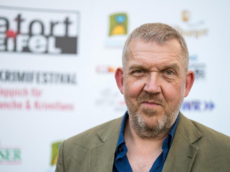 Schauspieler Dietmar Bär steht nach der Präsentation der Festivalweine für das Krimifestival "Tatort Eifel" vor einem Aufsteller.