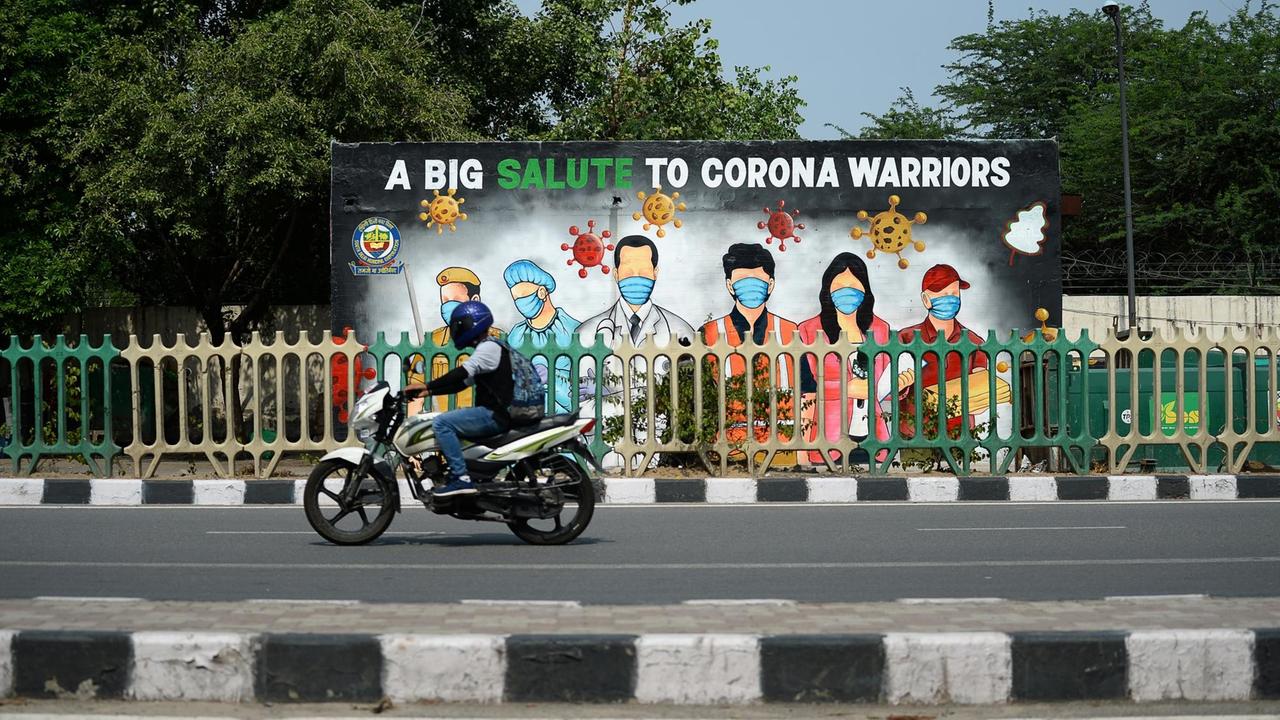 In Indiens Hauptstadt Neu Delhi würdigt ein Plakat den Kampf vieler Menschen gegen die Corona-Pandemie. Auf dem Plakat sind u.a. ein Arzt, eine Pflegerin und ein Polizist zu sehen. Darunter steht: "A big salute to corona warriors" ("Ein Gruß an die Corona-Kämpfer"). Ein Motorradfahrer fährt daran vorbei. In Indiens Hauptstadt Neu Delhi würdigt ein Plakat den Kampf vieler Menschen gegen die Corona-Pandemie. Auf dem Plakat sind u.a. ein Arzt, eine Pflegerin und ein Polizist zu sehen. Darunter steht: "A big salute to corona warriors" ("Ein Gruß an die Corona-Kämpfer"). Ein Motorradfahrer fährt daran vorbei.