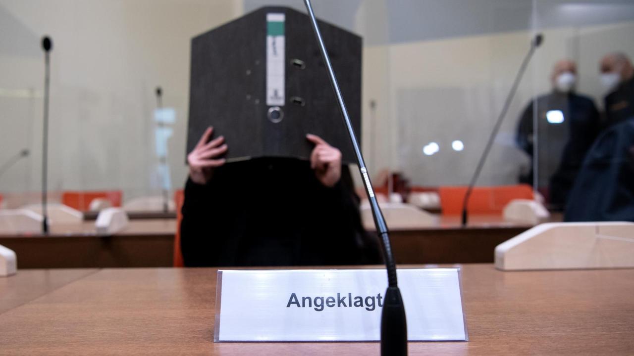 Jennifer W. sitzt im Saal von dem Gericht und hält sich einen Akten-Ordner vor das Gesicht. Jennifer W. sitzt im Saal von dem Gericht und hält sich einen Akten-Ordner vor das Gesicht.
