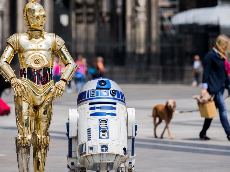 Die Roboter "C-3PO" (l) und R2-D2 aus den Star-Wars-Filmen als Wachsfiguren vor dem Kölner Dom.