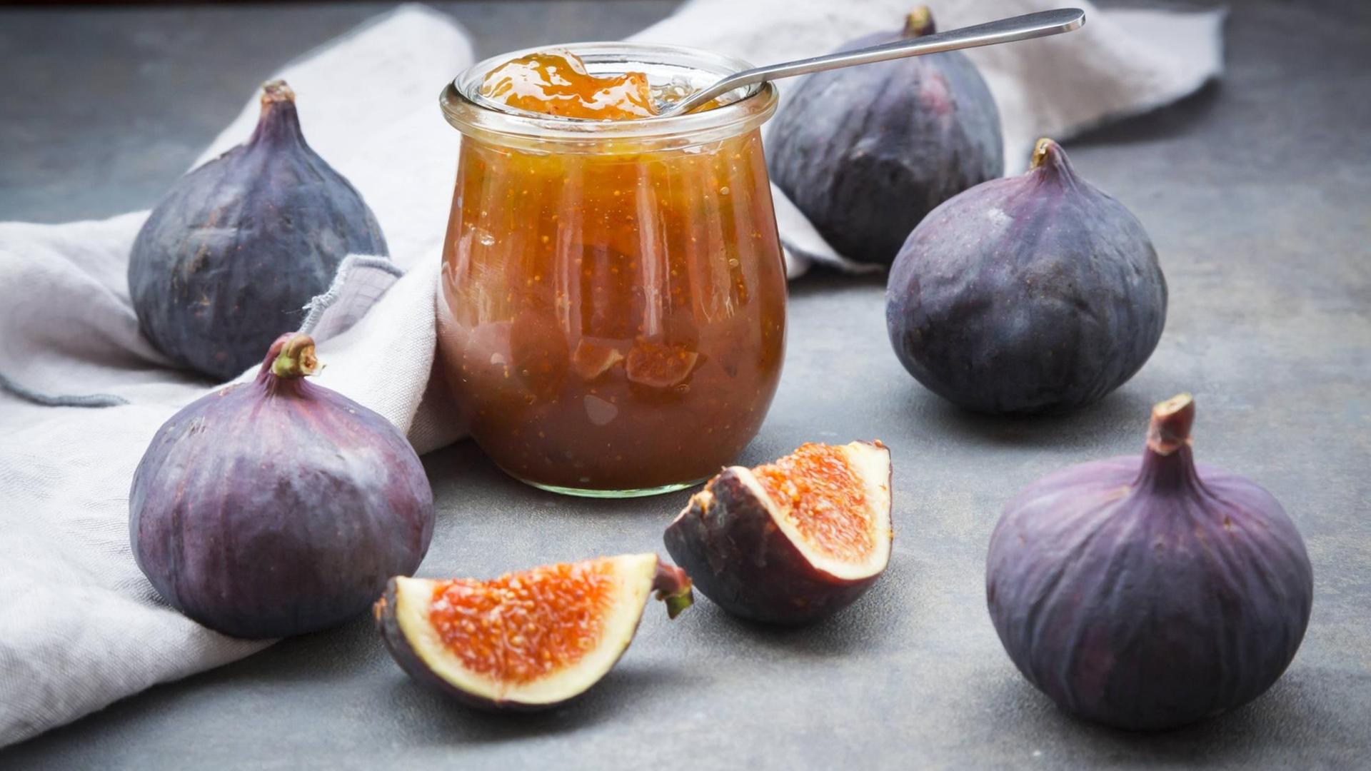 Feigen liegen auf einem Tisch, in der Mitte ein Glas Feigenmarmelade Feigen liegen auf einem Tisch, in der Mitte ein Glas Feigenmarmelade