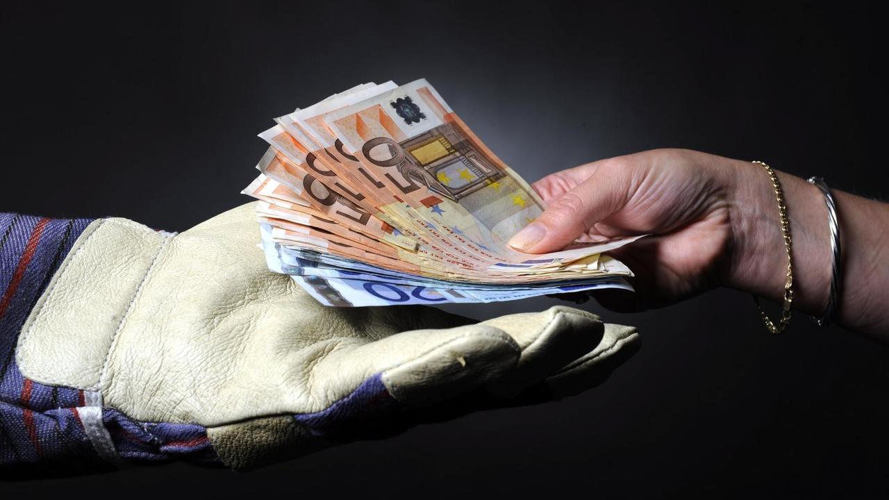 Eine Hand mit einem Arbeitshandschuh nimmt 560 Euro entgegen.