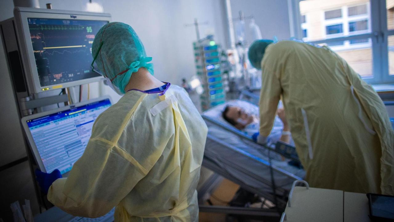 Zwei Krankenpfleger im Zimmer eines Patienten. Einer steht an einem Monitor, der andere beugt sich über das Bett. Beide tragen Kittel und Masken. Zwei Krankenpfleger im Zimmer eines Patienten. Einer steht an einem Monitor, der andere beugt sich über das Bett. Beide tragen Kittel und Masken.