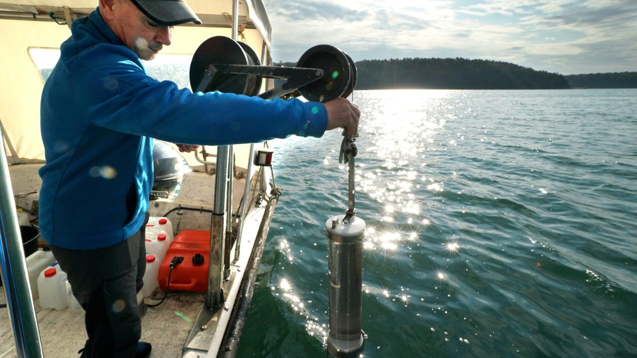 Auf einem Boot steht ein Mann, der einen Glaszylinder in der Hand hält. Auf einem Boot steht ein Mann, der einen Glaszylinder in der Hand hält.