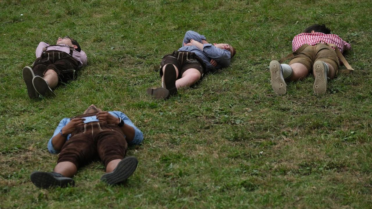 Enthusiasten in bayerischer Tracht und Lederhosen schlafen am zweiten Tag des Oktoberfestes 2019 auf einem Hügel in der Nähe von Bierzelten. Enthusiasten in bayerischer Tracht und Lederhosen schlafen am zweiten Tag des Oktoberfestes 2019 auf einem Hügel in der Nähe von Bierzelten.