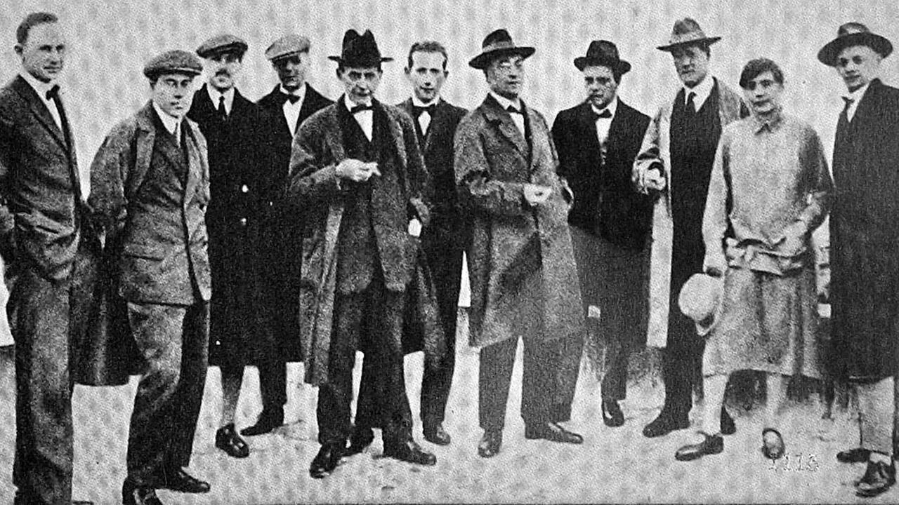 Eine Gruppe von Männern mit Hüten und eine Frau stehen für das Foto dicht beieinander.