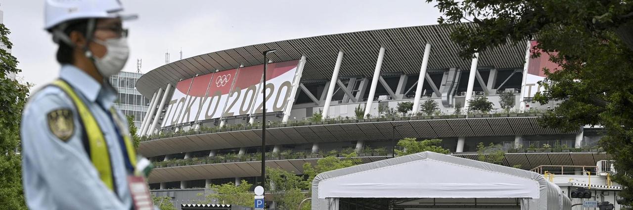 Ein Sicherheitsbeamter in Tokio trägt eine Schutzmaske und steht vor dem Nationalstadion.
Ein Sicherheitsbeamter in Tokio trägt eine Schutzmaske und steht vor dem Nationalstadion.