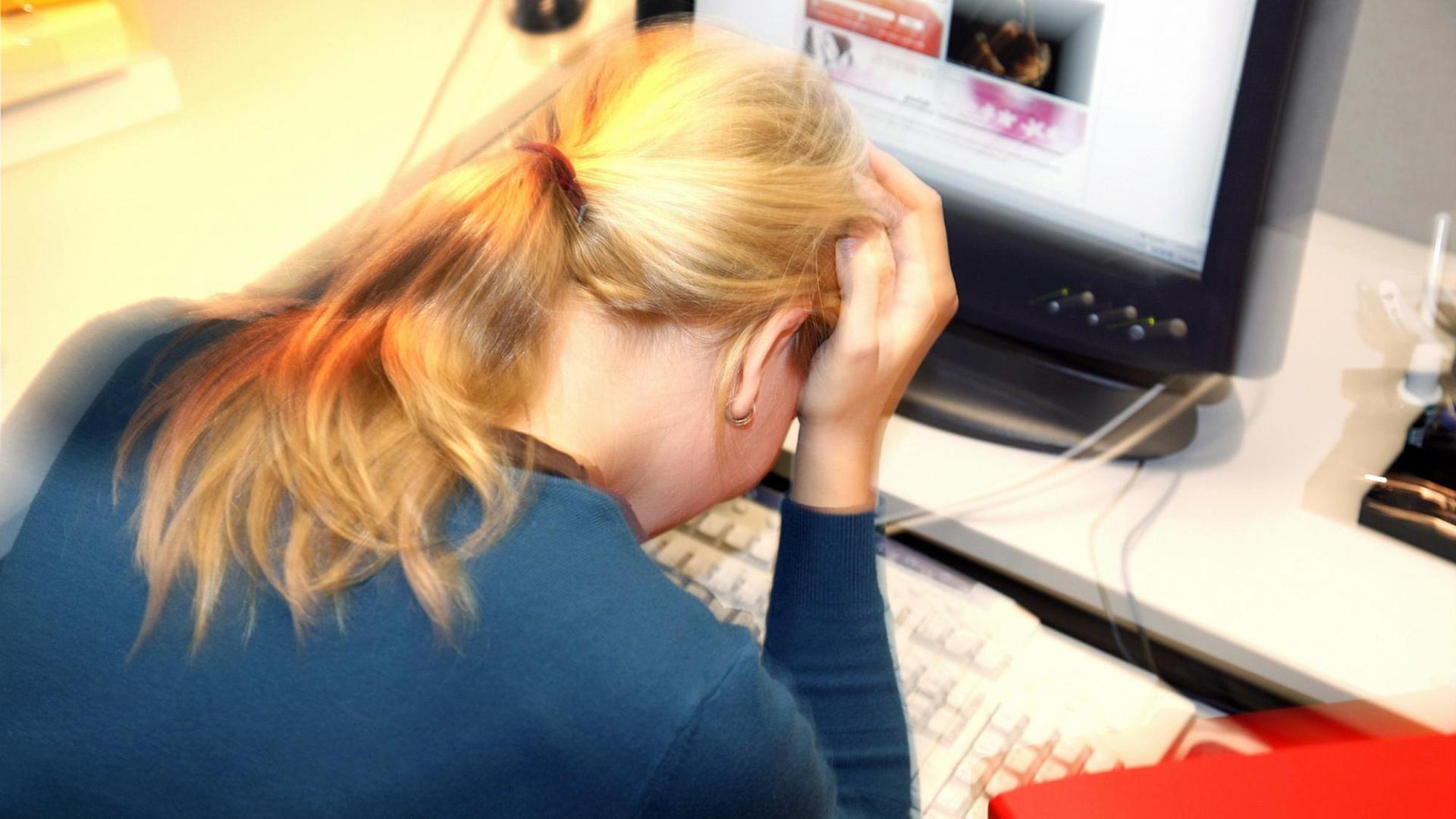 Eine Frau sitzt an einem Schreibtisch vor einem Computer, den Kopf auf die Hände gestützt. Eine Frau sitzt an einem Schreibtisch vor einem Computer, den Kopf auf die Hände gestützt.