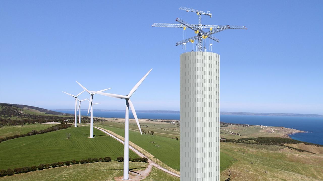 Hohe Kräne stapeln einen Turm aus großen Beton-Elementen aufeinander, im Hintergrund stehen Windräder Hohe Kräne stapeln einen Turm aus großen Beton-Elementen aufeinander, im Hintergrund stehen Windräder