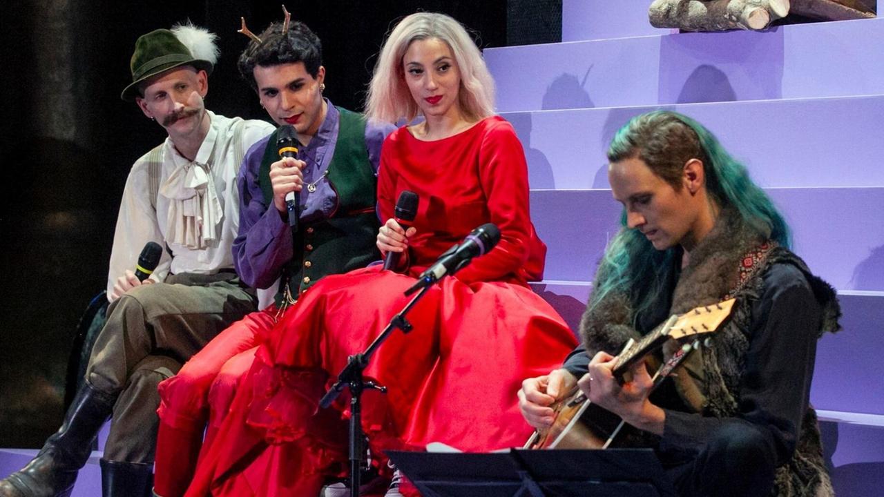 Die Schauspieler Damian Rebgetz, Benjamin Radjaipour, Zeynep Bozbay und Christian Löber sitzen auf einer Treppe auf der Bühne der Münchner Kammerspiele bei der Aufführung "Nirvanas Last". Löber spielt Gitarre während die anderen zusehen und Mikrofone in ihren Händen halten. Die Schauspieler Damian Rebgetz, Benjamin Radjaipour, Zeynep Bozbay und Christian Löber sitzen auf einer Treppe auf der Bühne der Münchner Kammerspiele bei der Aufführung "Nirvanas Last". Löber spielt Gitarre während die anderen zusehen und Mikrofone in ihren Händen halten.