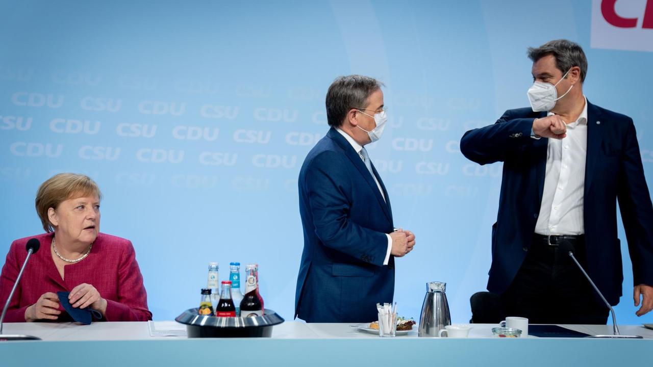 Armin Laschet, CDU-Bundesvorsitzender und Ministerpräsident von Nordrhein-Westfalen, und Markus Söder, CSU-Vorsitzender und Ministerpräsident von Bayern, begrüßen sich zu Beginn der Klausur der Spitzen von CDU und CSU zur Verabschiedung des Wahlprogramms für die Bundestagswahl neben Bundeskanzlerin Angela Merkel.
