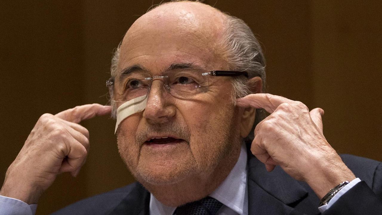 Joseph Blatter steckt sich bei einer Pressekonferenz die Zeigefinger in beide Ohren.