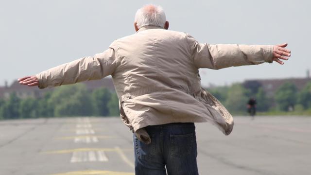 Ein älterer Mann läuft über das Tempelhofer Feld und breitet die Arme aus.