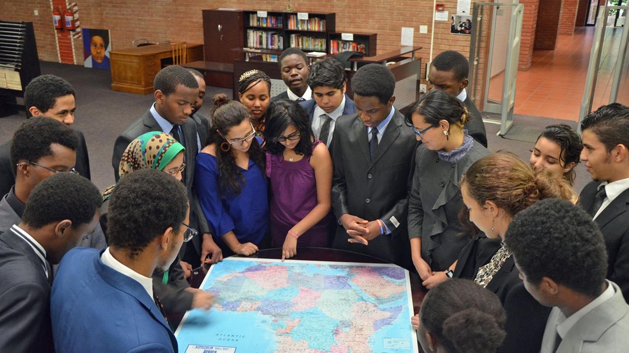 Eine Gruppe afrikanischer Studierender steht im Halbkreis und beugt die Köpfe über eine Afrika-Karte.