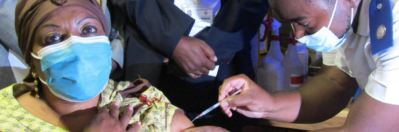 Die Gesundheitsminsterin von Namibia sitzt in einem gelben Kleid auf einem Stuhl und wird von einem Arzt geimpft Die Gesundheitsminsterin von Namibia sitzt in einem gelben Kleid auf einem Stuhl und wird von einem Arzt geimpft