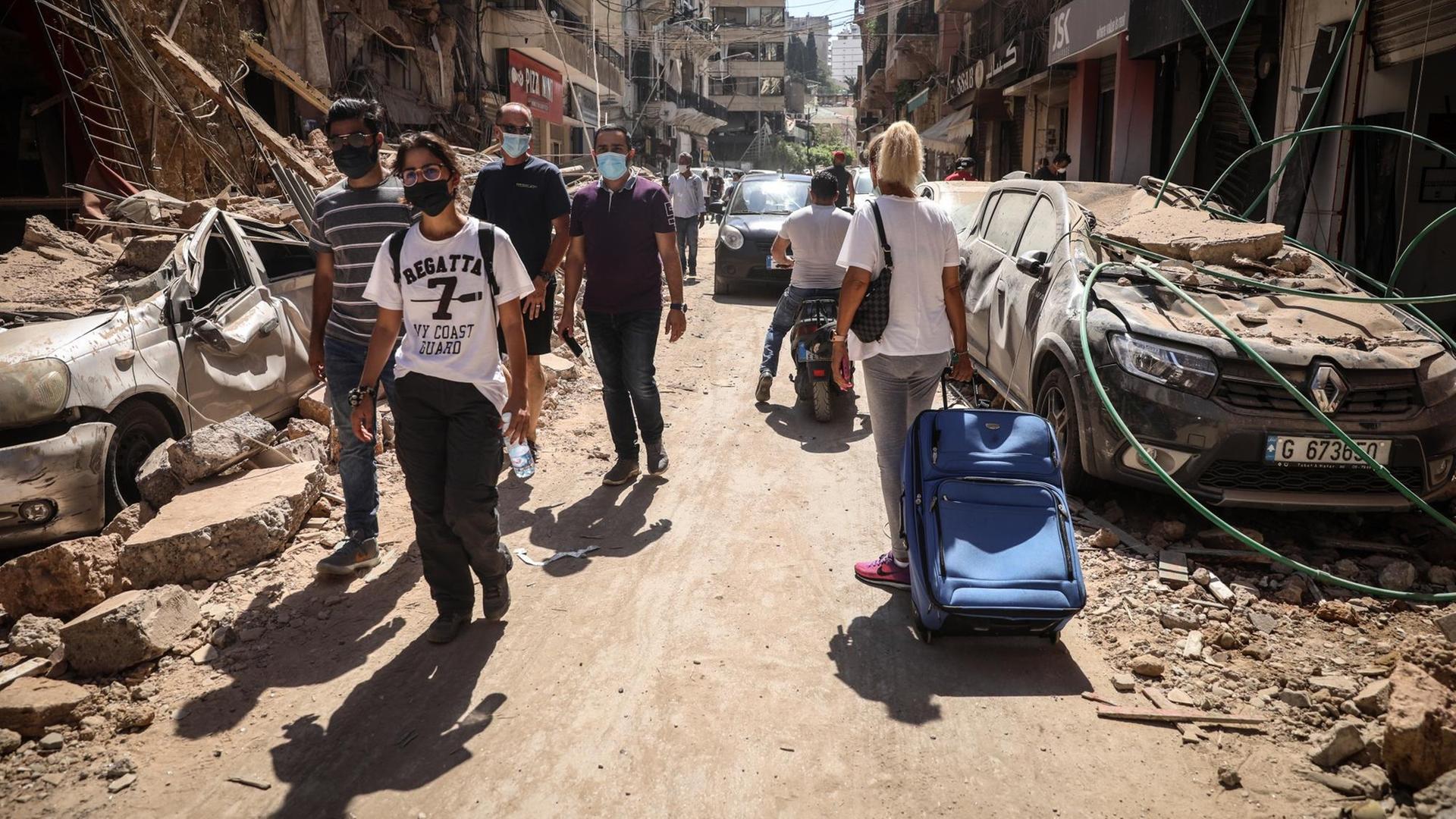 Menschen laufen durch eine zerstörte Straße in Beirut. Menschen laufen durch eine zerstörte Straße in Beirut.