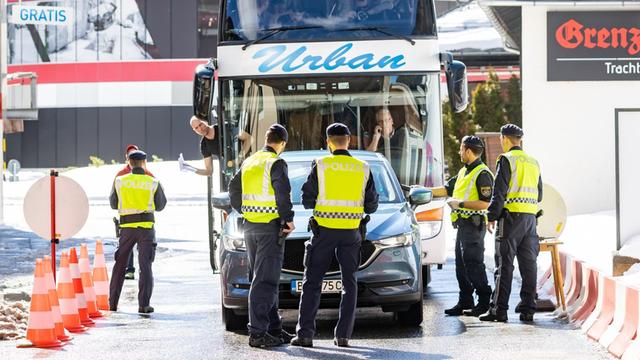 Polizisten führen Fahrzeugkontrollen durch. Mehrere Polizeibeamte stehen auf der Straße und halten einen doppelstöckigen Reisebus auf.
