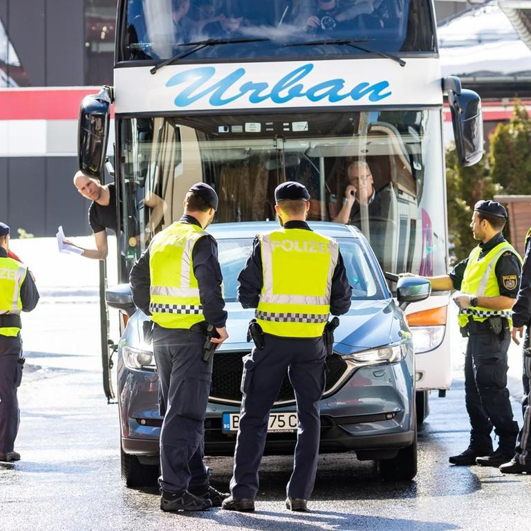 Polizisten führen Fahrzeugkontrollen durch. Mehrere Polizeibeamte stehen auf der Straße und halten einen doppelstöckigen Reisebus auf.