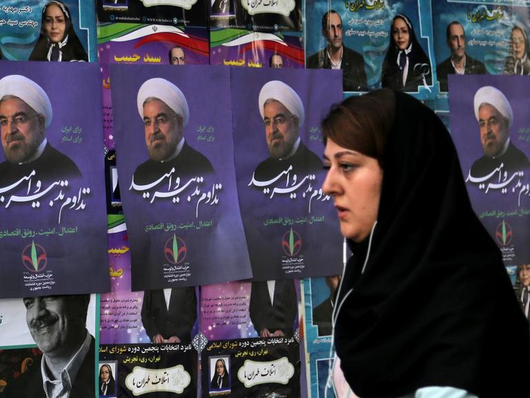 Eine iranische Frau läuft an Wahlplakaten von Irans Präsident Hassan Rohani vorbei