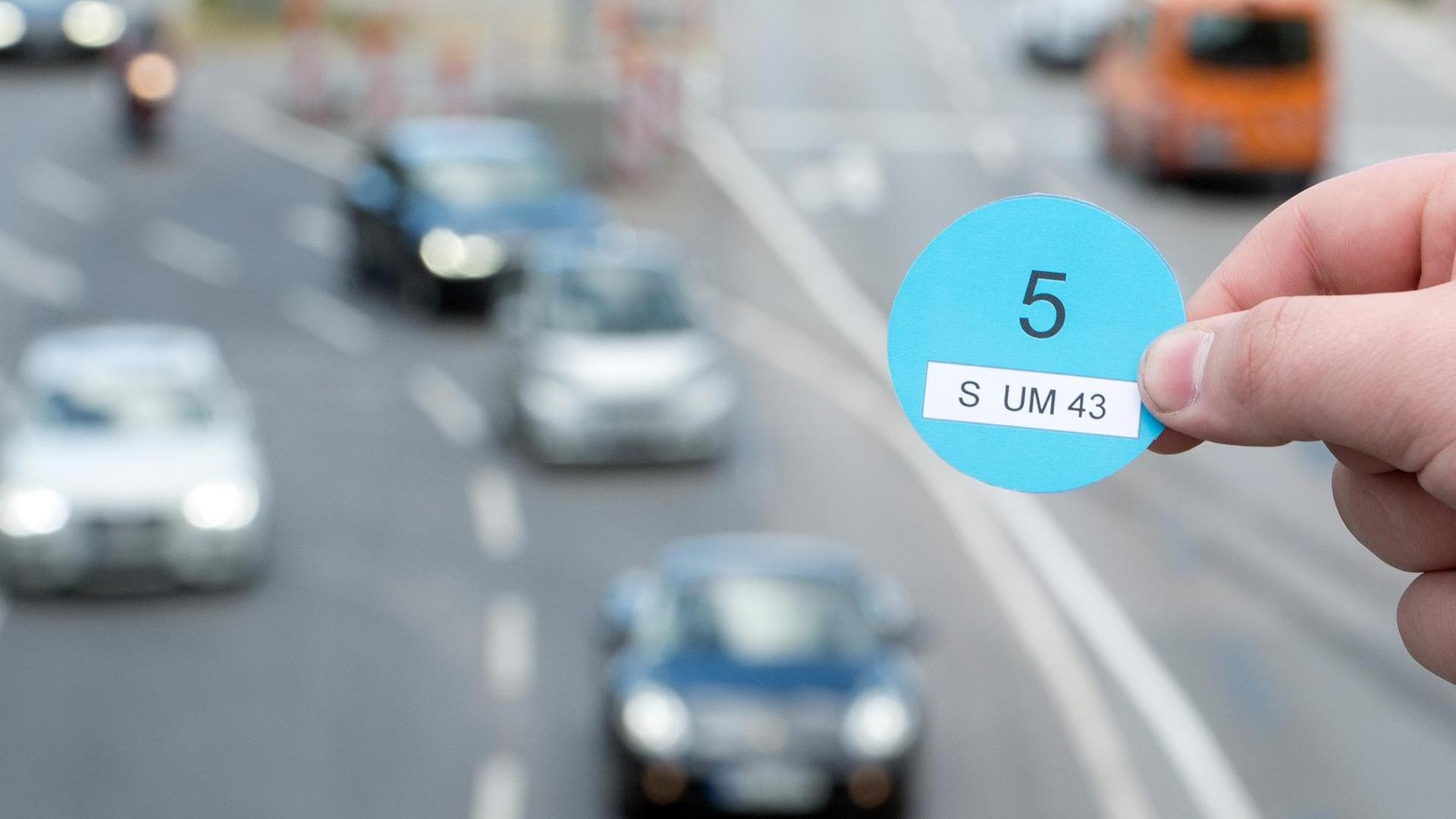 Eine Hand hält am 05.10.2016 einen Designvorschlag des Verkehrsministeriums Baden-Württemberg in der Innenstadt von Stuttgart (Baden-Württemberg) vor vorbeifahrenden Autos (gestellte Szene). Eine Hand hält am 05.10.2016 einen Designvorschlag des Verkehrsministeriums Baden-Württemberg in der Innenstadt von Stuttgart (Baden-Württemberg) vor vorbeifahrenden Autos (gestellte Szene).
