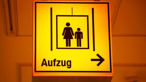 Ein gelbes Schild mit einer stilisierten Frau und einem Kind weist den Weg zu einem Fahrstuhl in einem Einkaufszentrum in Frankfurt, aufgenommen im März 2011.