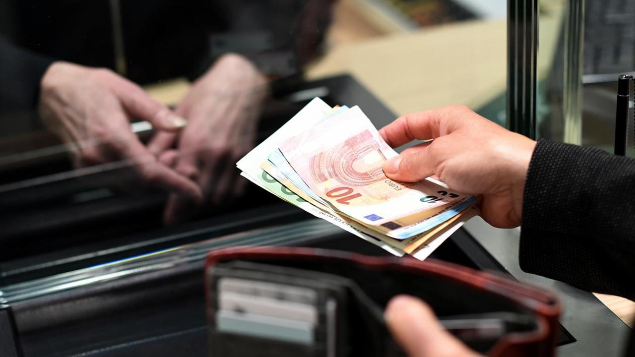 Zwei Hände mit Geldscheinen - eine Frau lässt sich in einer Bankfiliale am Schalter Bargeld auszahlen.