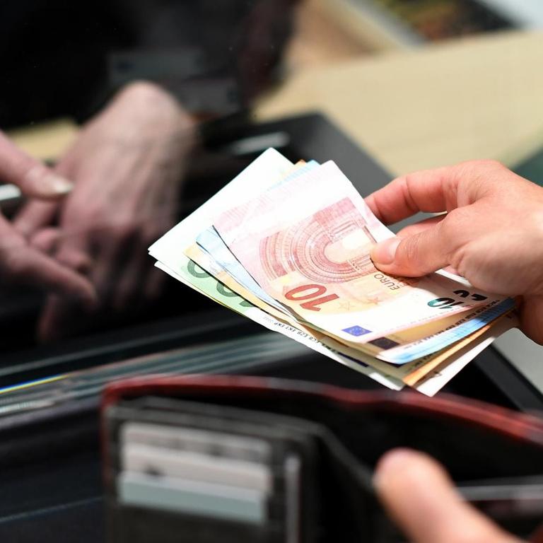 Zwei Hände mit Geldscheinen - eine Frau lässt sich in einer Bankfiliale am Schalter Bargeld auszahlen.