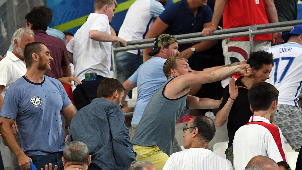 Das Bild zeigt mehrere Hooligans und viele flüchtende Fans; in der Bildmitte schlägt einer der Hooligans einem Zuschauer mit der Faust in den Nacken. Das Bild zeigt mehrere Hooligans und viele flüchtende Fans; in der Bildmitte schlägt einer der Hooligans einem Zuschauer mit der Faust in den Nacken.