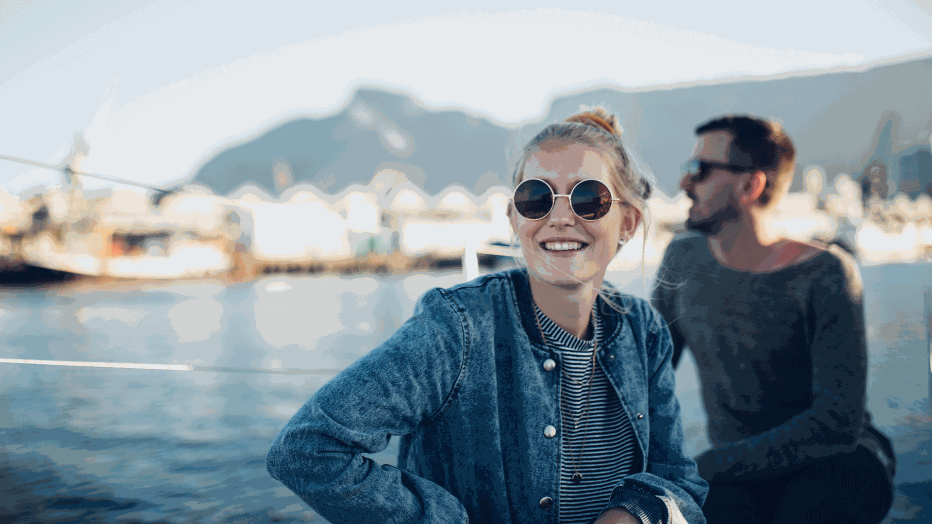Frau und Mann sitzen auf einem Kreuzfahrtschiff, im Hintergrund ein Hafen. Frau und Mann sitzen auf einem Kreuzfahrtschiff, im Hintergrund ein Hafen.