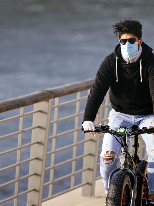 Ein Radfahrer mit Atemschutzmasker am Rheinboulevard in Köln.
