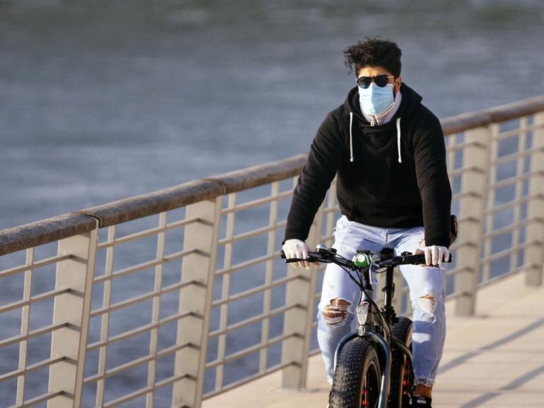Ein Radfahrer mit Atemschutzmasker am Rheinboulevard in Köln.