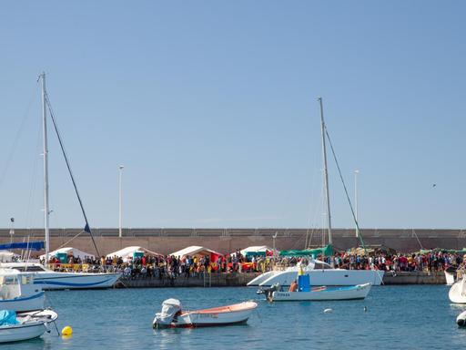 Blick auf den Hafen von Arguineguín. Im Hafenbecken Boote, an Land Zelte, an denen sich Menschen drängen.