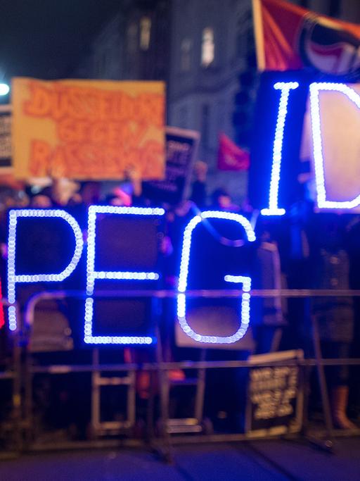 Gegner der Anti-Islam-Bewegung "Dügida" demonstrieren am 12.01.2015 in Düsseldorf (Nordrhein-Westfalen) mit einer Leuchtschrift "Stop PEGIDA"