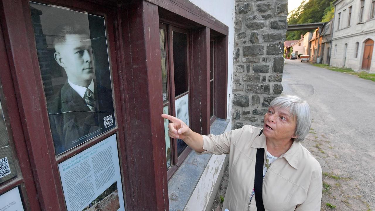 Neben einem Porträtfoto ihres Großvaters Hans Riedel steht Gisela Heiden am Eingang zum ehemaligen KZ Sachsenburg in Frankenberg (Sachsen). Neben einem Porträtfoto ihres Großvaters Hans Riedel steht Gisela Heiden am Eingang zum ehemaligen KZ Sachsenburg in Frankenberg (Sachsen).