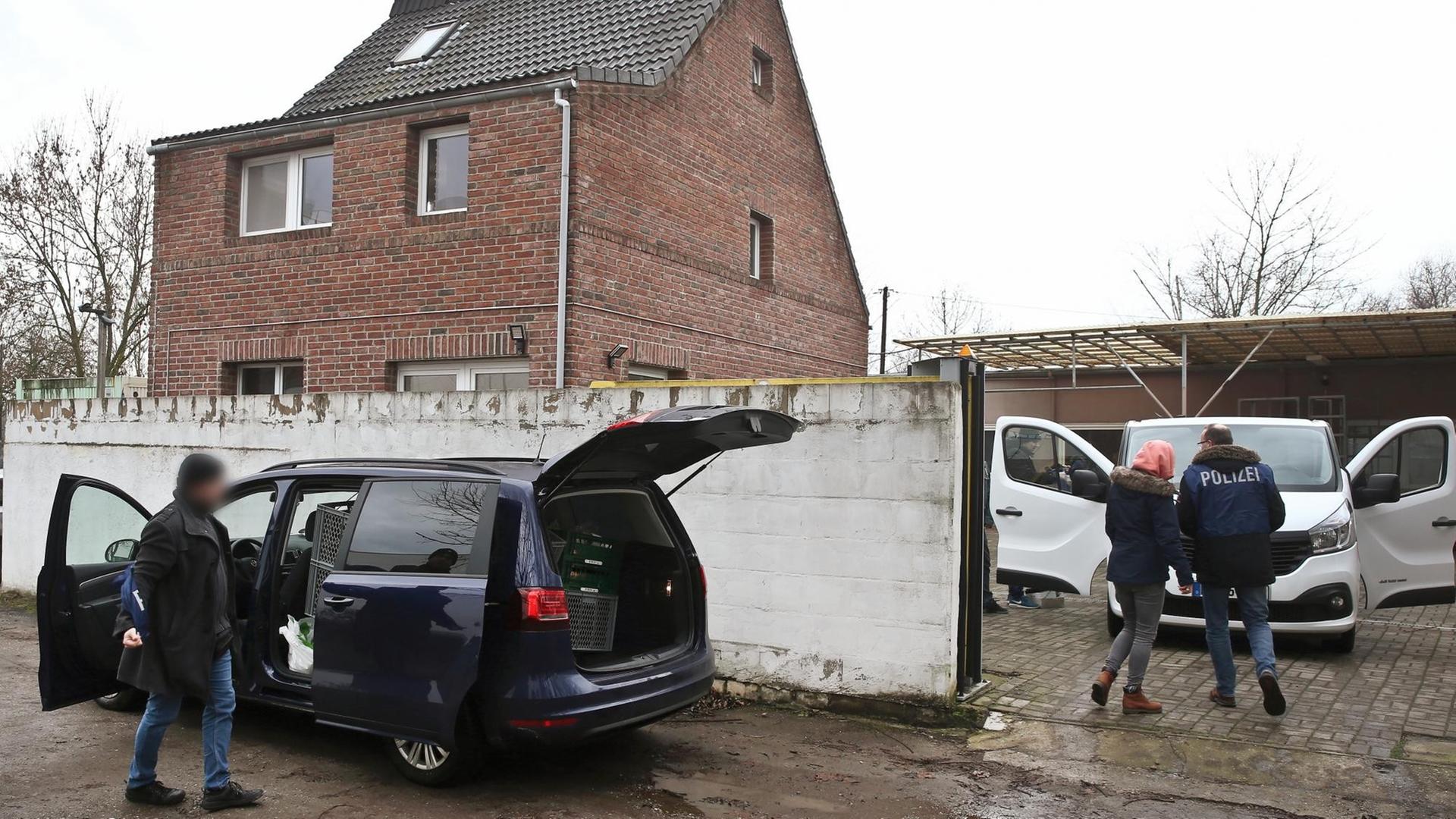 Polizeibeamte stehen vor einem Haus in Neuss. Dazu ein dunkelblaues Auto mit geöffneten Türen. Polizeibeamte stehen vor einem Haus in Neuss. Dazu ein dunkelblaues Auto mit geöffneten Türen.