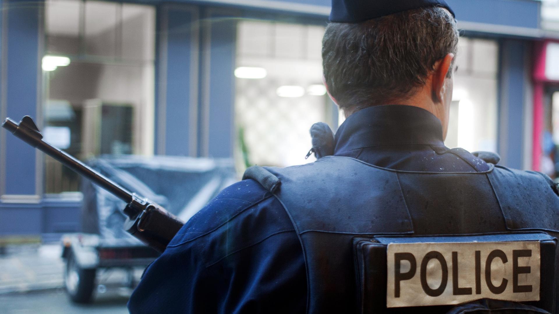 Ein bewaffneter Polizist steht in Paris vor einer Häuserzeile. Ein bewaffneter Polizist steht in Paris vor einer Häuserzeile.