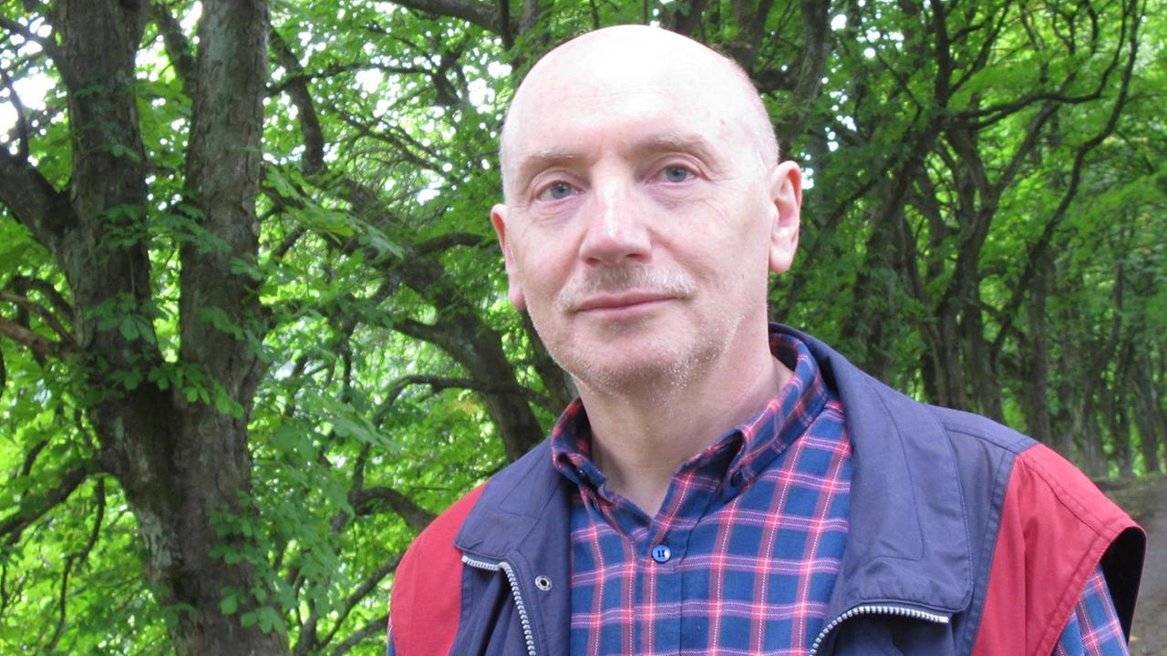 Porträt des Publizisten und Übersetzers Hans-Günter Wagner mit blau-roter Anglerweste und kariertem Hemd in einer Allee grün belaubter Bäume Porträt des Publizisten und Übersetzers Hans-Günter Wagner mit blau-roter Anglerweste und kariertem Hemd in einer Allee grün belaubter Bäume