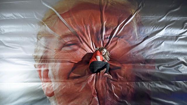 Eine Frau lieget auf einer großen Sprung-Luftmatratze, auf die das Gesicht von Donald Trump aufgedruckt ist.