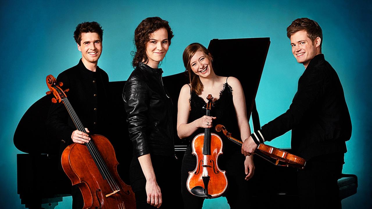Vier Musiker stehen mit ihren Instrumenten vor einem petrol-blauen Hintergrund. Vier Musiker stehen mit ihren Instrumenten vor einem petrol-blauen Hintergrund.